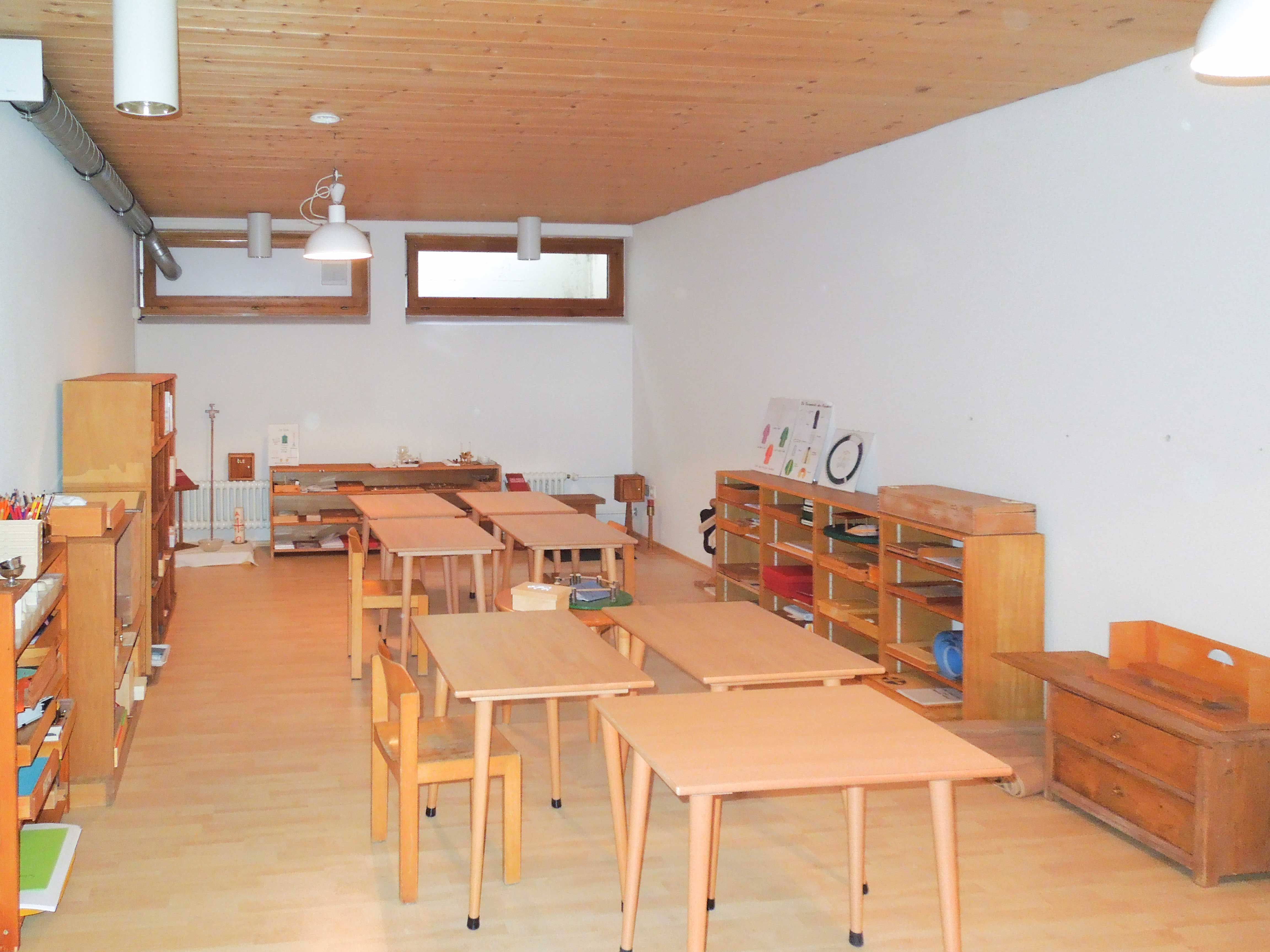 In diesem Atrium Stufe eins sind kleine Tische in der Mitte und Regale an den Wänden mit Materialien, mit denen die Kinder arbeiten können.